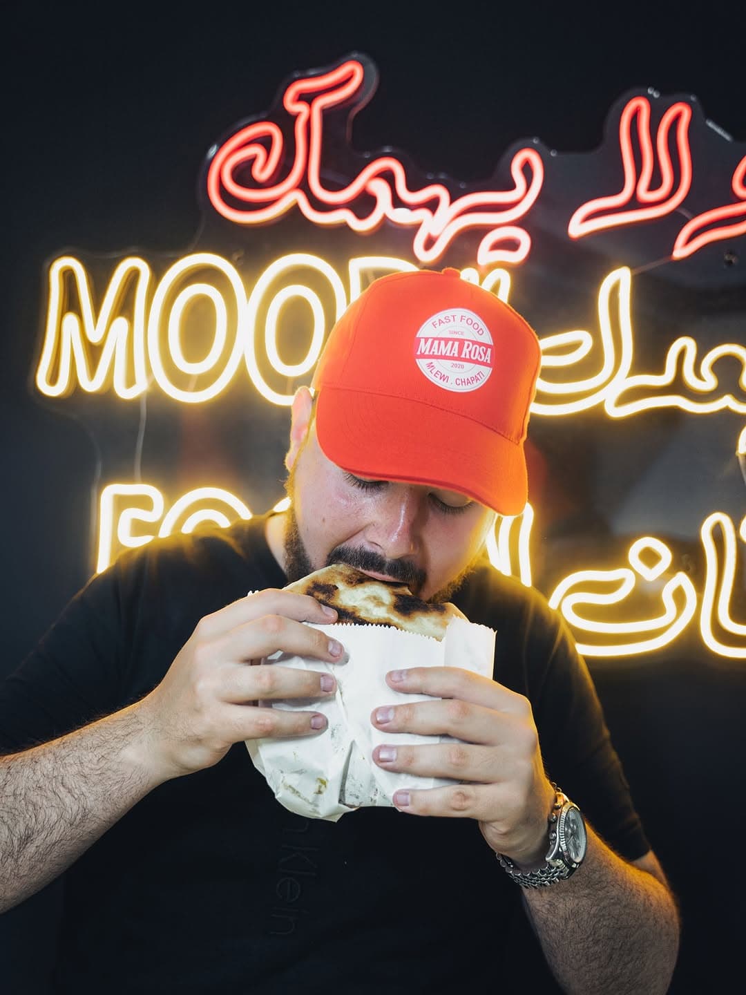 Customer enjoying a delicious Mama Rosa sandwich with neon signage in background