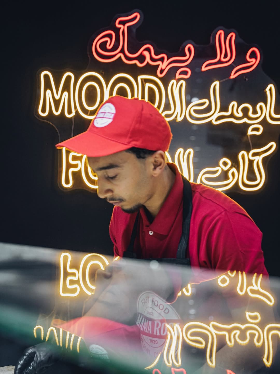 Team member working behind the counter with Arabic neon signage visible